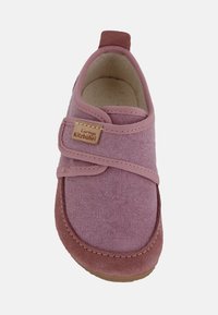 Różowy materiałowy but z miękkim zamszowym noskiem i piętą, wyposażony w rzep oraz jasnobrązową metkę z napisem "Living Kitzbühel." Okrągły kształt.