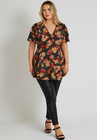 Blommig tunika med korta ärmar, med en svart bakgrund och orange/röda blommor; kombinerad med svarta leggings i imiterat läder och klackar med remmar.