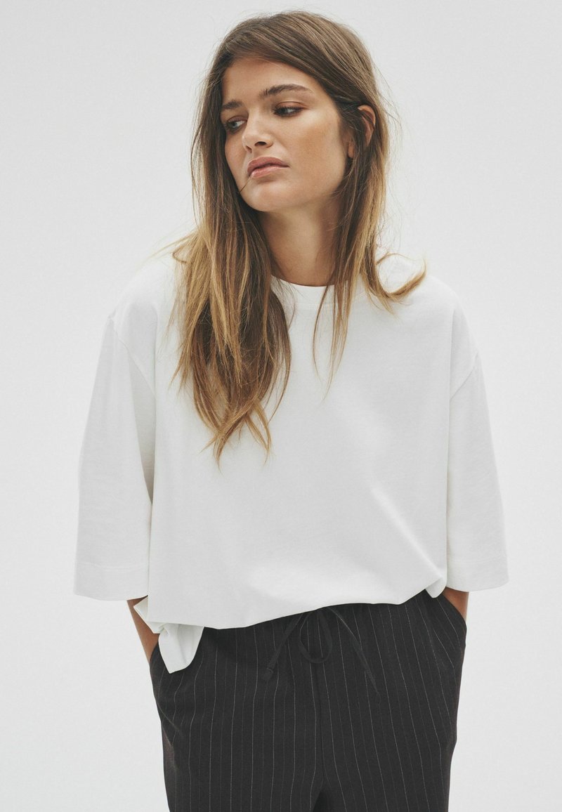 Biała, oversize koszulka z miękkiej bawełny, z okrągłym dekoltem i zwisającymi rękawami, w połączeniu z czarnymi spodniami w prążki.