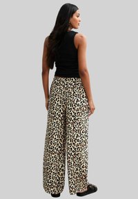 Leopardenmuster-Hose mit weitem Bein und beigem Grundton, aus leichtem Stoff und mit elastischem Bund, kombiniert mit einem schwarzen ärmellosen Oberteil.