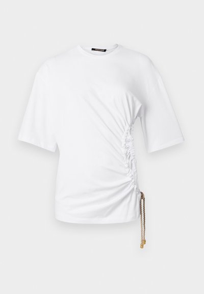 Valge lühikeste varrukatega T-särk külgede volangidega ja reguleeritava pikkusega drawstringiga, millel on kuldne metallist detail. Sile puuvillane kangas.