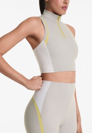 Top corto sportivo in grigio chiaro con colletto a zip e dettagli gialli, abbinato a leggings grigi a vita alta e sagomati.
