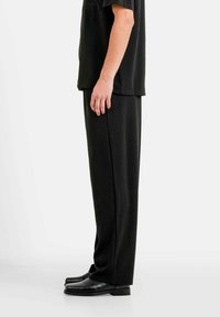 Pantalon noir et chemise assortie présentés en vue latérale. Coupe ample, texture lisse et couleur unie. La chaussure affiche un design épuré.
