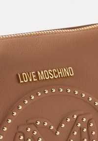 Braune Ledertasche mit einem goldenen "LOVE MOSCHINO"-Logo und dekorativen goldenen Nieten in einem kreisförmigen Muster auf der Oberfläche. Mit Reißverschluss.