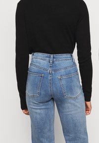 Jeans in denim blu a vita alta con un lavaggio sbiadito, dotati di due tasche posteriori e chiusura con zip. Il materiale ha una leggera elasticità.