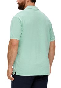 Miętowa koszulka polo o teksturowanym wykończeniu, z krótkimi rękawami i rozcięciami po bokach na dole. Standardowy kołnierzyk i luźny krój.