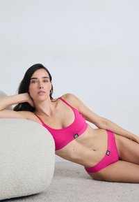 Rosa ribbet bralette og matchende bikini-bunn, med et lite svart logotag; glatt tekstur, sømløs design og ingen synlige mønstre.
