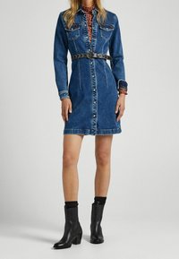 Jeansklänning, knappar framtill, krage, långa ärmar, smal svart bälte, knä-lång. Matchas med svarta läderankelstövlar.