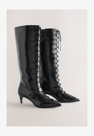 Stivali neri in pelle fino al ginocchio con punta appuntita, caratterizzati da una chiusura con lacci sul lato, tacco basso a kitten heel e chiusura con cerniera.
