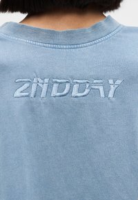 Φωτεινό γαλάζιο βαμβακερό φούτερ με στρογγυλή λαιμόκοψη και κεντημένο κείμενο "2NDDAY" στην πλάτη με νήμα σε λίγο πιο σκουρό μπλε χρώμα.