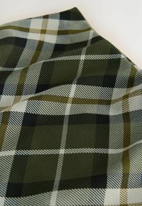 Kariertes Gewebe in dunklem Grün, Schwarz und Weiß mit feinen Texturen und kontrastierenden Linien, die ein markantes Muster erzeugen.