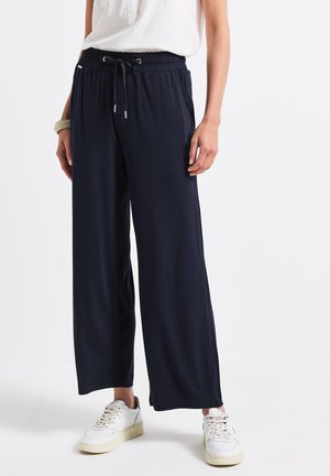 Himmelblaue weit geschnittene Hose aus weichem Stoff, mit einem elastischen Bund und Kordelzug. Die Hose wird mit weißen Sneakers kombiniert.