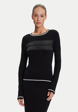 Dolcevita nero a maniche lunghe con un motivo orizzontale di cristalli sul petto e rifiniture bianche sul colletto e sui polsini. Texture liscia.