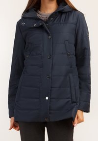 Mörkblå vadderad jacka med dragkedja och knappstängning, huva, sidofickor och quiltad textur. Har silverfärgade detaljer.
