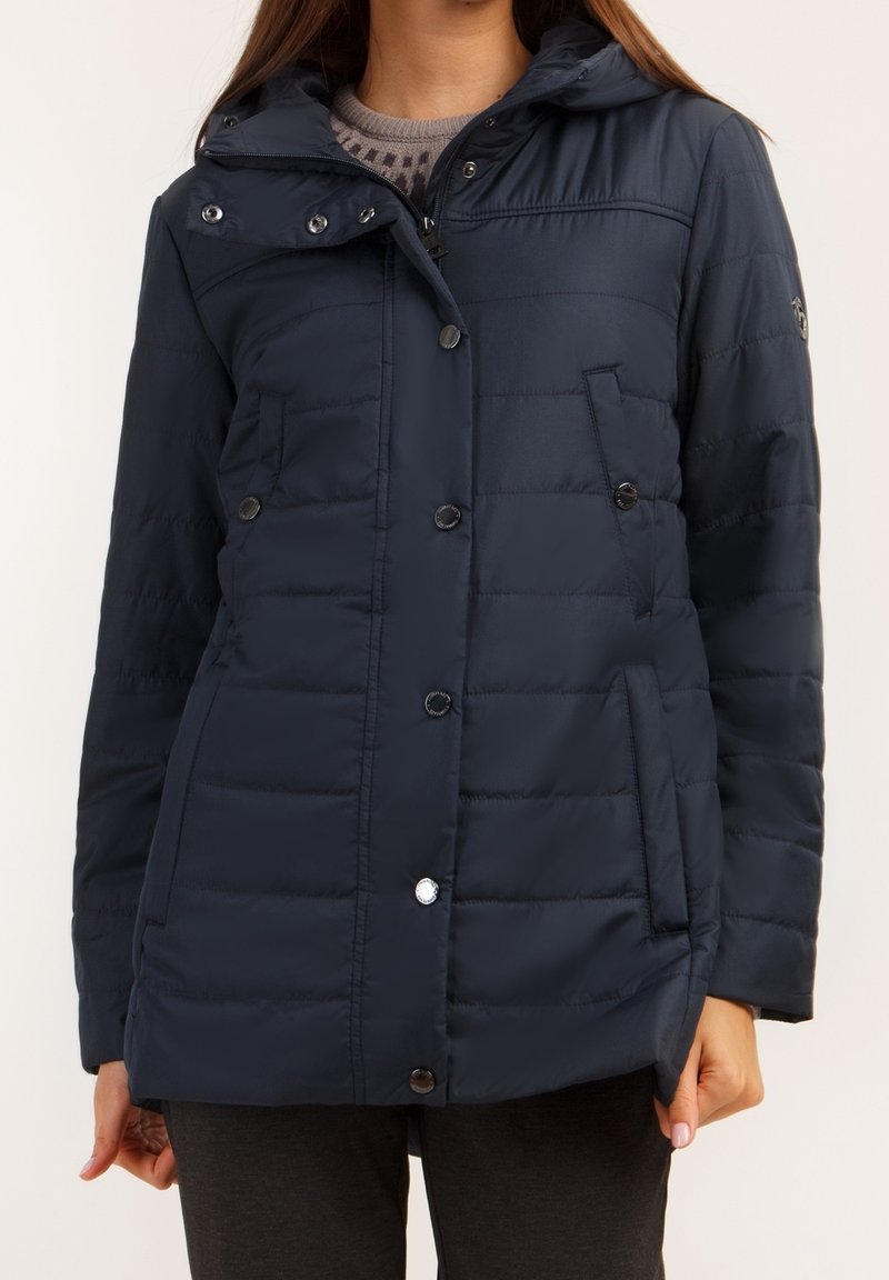 Mörkblå vadderad jacka med dragkedja och knappstängning, huva, sidofickor och quiltad textur. Har silverfärgade detaljer.