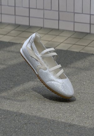 Bílá bota s prasklou texturou, s výřezy a třemi pásky přes přední část. Pryžová podrážka s hnědým spodním okrajem.