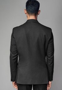 Dunkelgraue maßgeschneiderte Anzugjacke aus strukturiertem Stoff, mit einem Schlitze und drei schwarzen Knöpfen an jedem Ärmel. Die Rückansicht zeigt eine figurbetonte Silhouette.
