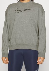 Felpa grigia realizzata in tessuto morbido, con collo a giro e spalle scese, caratterizzata dal logo Nike swoosh nero sulla parte anteriore.
