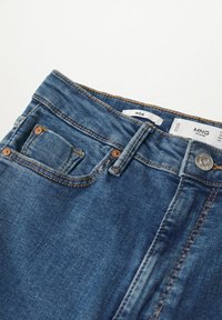 Jean en denim bleu montrant le haut avant avec bouton, passants de ceinture, poche avant et étiquettes intérieures portant les mentions "MNG Denim" et "NOA".