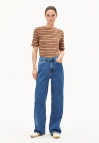Bruin gestreept T-shirt met korte mouwen, gecombineerd met hooggeplaatste wijde blauwe jeans en lichtgekleurde schoenen. Schone, casual uitstraling.
