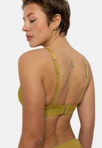 Soutien-gorge en dentelle et tissu vert olive avec des bretelles ajustables, fermeture à crochets et œillets, et une bordure décorative en dentelle le long de la bande.