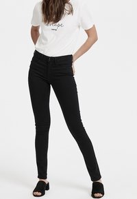 Černé džíny skinny s těsným střihem, doplněné bílým tričkem s černým nápisem a černými sandály na blokovém podpatku s otevřenou špičkou.