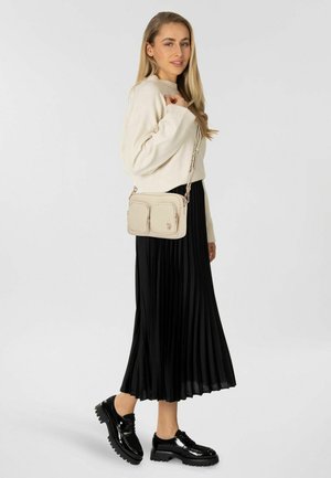 Beige crossbodytas met twee voorvakken, zilverkleurige beslag en een doorgestikt ontwerp, gecombineerd met een zwarte geplooide rok en glanzende zwarte schoenen.