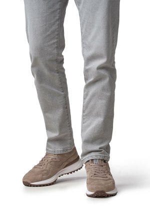 Baskets en daim marron avec un design texturé et semelles en caoutchouc blanches ; associées à un jean gris clair ajusté, montrant une silhouette élancée.