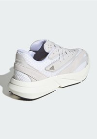 Zapatilla gris claro con paneles de malla y ante, suelas acolchadas, cordones planos y suela de goma. Presenta un diseño texturizado y un acento de marca.