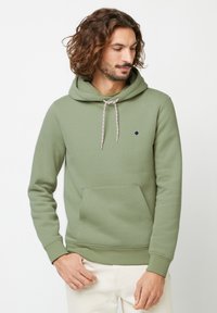 Groene katoenen hoodie met een trekkoord in de capuchon, een buidelzak en een klein geborduurd boomlogo op de borst. Zachte textuur, casual pasvorm.