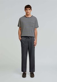 Cămașă cu mânecă scurtă în dungi, navy și crem, asortată cu pantaloni cu șnur gri închis. Ambele articole au o croială lejeră și un design casual.