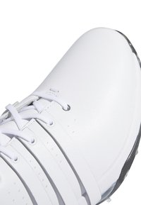 Bílé sportovní boty s hladkým syntetickým svrškem, šesti dírkami na tkaničky a strukturovanou podrážkou s černými akcenty. Minimalistický design a čisté linie.