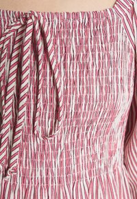 Gros plan d’un tissu rayé vertical rose et blanc avec coutures élastiques froncées et un petit détail de nœud noué.