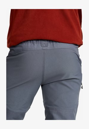 Close-up of a person wearing gray pants and a red fleece jacket, showing stitching and waistband details.