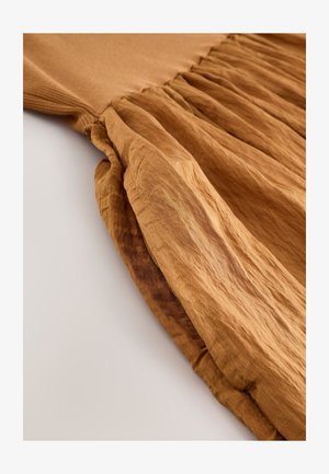 Hnědé šaty z texturované, mačkané látky s přiléhavým živůtkem a plisovanou sukní. Viditelné švy podél lemu.