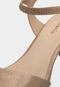 Μπεζ πέδιλο με ανοιχτά δάχτυλα, υφασμένες λουρίδες και χαμηλό χοντρό τακούνι, σε λευκό φόντο.