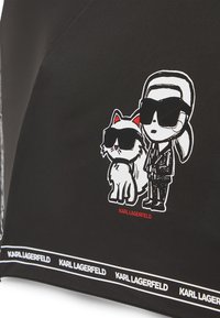 Black fabric umbrella featuring a cartoon design of a person and a cat, both in sunglasses. "KARL LAGERFELD" logo in white along the edge.