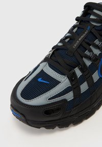 Nike-sneaker med ovandel i mesh i marinblått och grått, med svarta accenter och blå logodetalj; texturerad yta med ett distinkt snörningssystem.