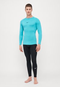 Lyseblå langærmet træningsshirt med sort Nike-logo, parret med sorte tætsiddende leggings med hvidt Nike-logo nær kanten.