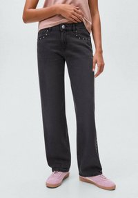 Črne široke kavbojke s visokim pasom, ki imajo okrasne stude na sprednjih žepih. Ujemajo se z roza supergami in nevtralno majico.