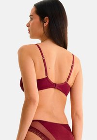 Soutien-gorge bordeaux avec bretelles ajustables, accents en dentelle et fermeture à crochets au dos ; texture de tissu douce et sans coutures.