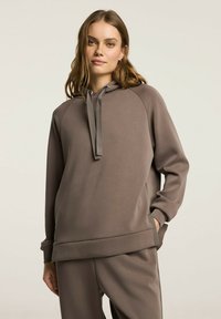 Brązowa bluzka z kapturem z raglanowymi rękawami, z detalami w postaci sznurków, o miękkiej fakturze, charakteryzująca się luźnym krojem i bocznymi kieszeniami.