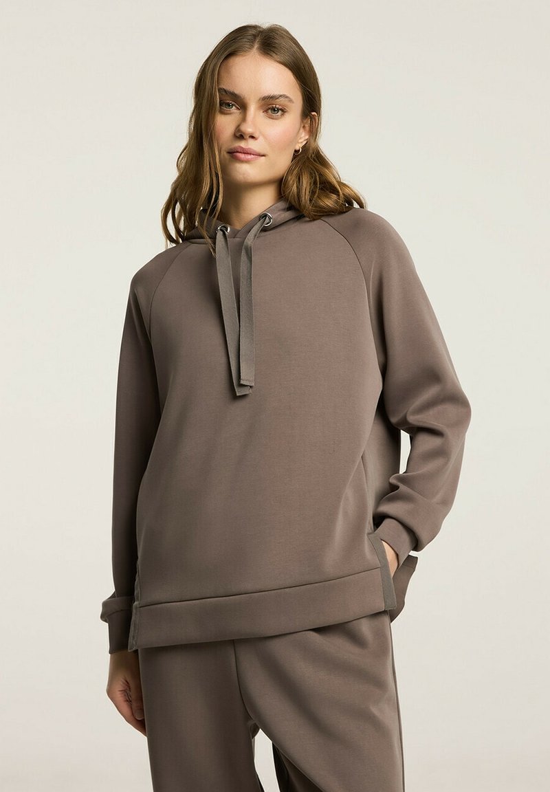 Brązowa bluzka z kapturem z raglanowymi rękawami, z detalami w postaci sznurków, o miękkiej fakturze, charakteryzująca się luźnym krojem i bocznymi kieszeniami.