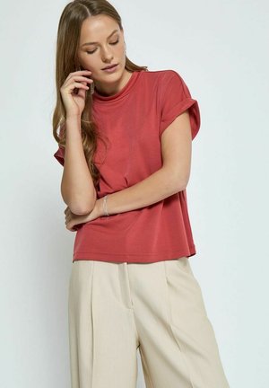 Top corto a maniche corte di rosso rosato in tessuto morbido, abbinato a pantaloni a vita alta beige chiaro con pieghe.