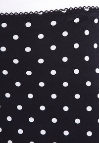 Tissu noir à pois blancs, avec une surface texturée et une délicate dentelle le long du bord supérieur.