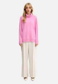 Maglione a collo alto rosa con polsini e orlo a coste, abbinato a pantaloni a gamba larga color crema e décolleté bianchi a punta.