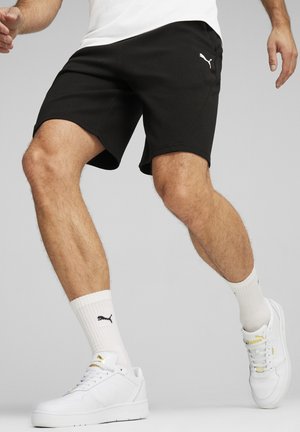 Czarne spodenki sportowe o gładkiej fakturze, z białym logo. Noszone z białymi trampkami i skarpetkami, podkreślają casualowy sportowy wygląd.