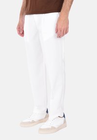 Pantaloni bianchi su misura con pieghe frontali, realizzati in tessuto morbido. Abbinati a sneakers bianche con accenti beige e blu navy.