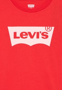 Červené bavlněné tričko s velkým bílým logem Levi's umístěným na hrudi, se klasickým designem krátkých rukávů a kulatým výstřihem.