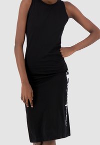 Czarna sukienka na ramiączkach wykonana z miękkiego, elastycznego materiału. Posiada dopasowaną sylwetkę z białym graficznym detalem z boku.